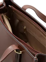 Cartera tipo shopper de cuero liso color marrón, con doble asa superior, correa ajustable y extraíble, herrajes metálicos dorados y logo de la marca en la parte frontal. Cuenta con cierre superior y múltiples compartimentos.