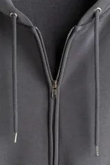 Campera con capucha de felpa gris oscuro, con interior cepillado suave. Modelo de hombros caídos, cierre frontal, bolsillos canguro delanteros y puños y bajo en punto acanalado.