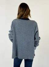 Saco de punto color naranja con detalles de rayas horizontales en las mangas y franjas verticales en el cuerpo. Tiene cuello tipo polo, cierre frontal con botones y un bolsillo decorativo en el pecho.