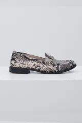 Mocasín de mujer con diseño de piel de serpiente en tonos blanco y negro. Presenta un detalle de estribo metálico en el empeine y una suela plana de color negro.