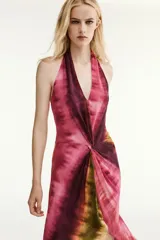 Vestido midi de cuello halter y escote en V, con diseño tie-dye en tonos fucsia, borgoña y verde. Presenta un nudo decorativo en el delantero, espalda descubierta y abertura frontal en el bajo.