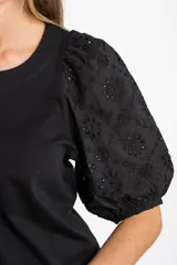 Remera de algodón color rosado con mangas cortas abullonadas de broderie con diseño floral calado. Presenta cuello redondo y costura vertical central en el frente.