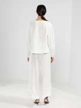 Camisa de lino con cuello en V y cierre frontal de botones. Presenta un diseño de silueta relajada, dobladillo curvado y mangas largas con puños elásticos.