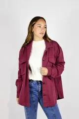 Camisa de gabardina bordó de corte oversize, con bolsillos frontales con solapa y cierre de botones oscuros.
