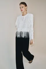 Chaqueta de cuello redondo y manga larga con hombreras, completamente cubierta de flecos con lentejuelas. Cuenta con forro interior y cierre frontal.