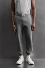 Pantalón jogger gris de corte regular fit, confeccionado en tejido de algodón con interior afelpado. Cuenta con cintura elástica ajustable con cordón, bolsillos laterales de vivo y traseros de plastrón. Presenta un texto estampado en color bordó en la pernera y bajo acabado en puño con elástico. Incluye un parche con logo combinado a contraste en la cintura.