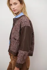 Chaqueta bomber color bordó con mangas de cuero sintético marrón y cuerpo de tweed con patrón de espiga. Cierre frontal con botones a presión y cuello redondo.