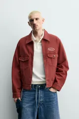 Cazadora cropped fit de Zara confeccionada en tejido de algodón con estructura canvas, de color bordó con efecto lavado. Cuenta con cuello solapa, manga larga con puños abotonados, bolsillos frontales de plastrón con solapa, parche bordado en el pecho y cierre frontal con cremallera.