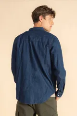 Camisa de jean azul de manga larga, con cierre frontal de botones a presión, dos bolsillos frontales con solapa y costuras reforzadas.