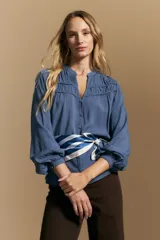 Camisa de manga larga color blanco, con cuello mao y escote en V. Presenta frunces en el canesú, cierre frontal con botones y mangas amplias con puños abotonados.