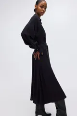 Vestido camisero midi negro de corte holgado, con cuello, escote en V y cierre frontal de botones dorados. Cuenta con mangas largas abullonadas con puños anchos y un lazo ajustable para atar en la cintura.