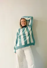 Sweater de punto con diseño de rayas verticales en tonos azul y gris, con sutil acabado brillante. Presenta cuello redondo, mangas largas con puños ajustados y corte amplio con aberturas laterales en el ruedo.