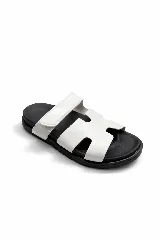 Sandalias planas con capellada blanca en forma de H y ajuste de velcro lateral. Poseen base de goma negra ergonómica.
