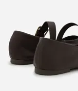 Zapatilla tipo bailarina de cuero negro, con punta redondeada, tacón bajo y una tira decorativa en el empeine con hebilla metálica dorada.