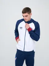 Campera deportiva Umbro del Club Nacional de Football, modelo con capucha, cierre frontal, bolsillos laterales y mangas raglán. Diseño en color blanco con mangas y detalles en azul marino y rojo.