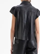 Camisa de cuero ovino color gris claro, con cuello camisero, volados centrales y mangas cortas con volumen generado por frunces en la copa. Cierre frontal con broches forrados.