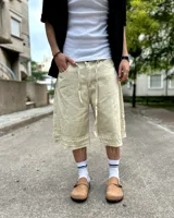 Bermuda de corte baggy color beige crema, con costura vertical trasera en cada pierna y detalle artesanal visible en el bajo. Incluye un cordón extra confeccionado en la misma tela.