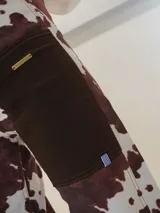 Pantalón vaquero de corte recto con estampado animal print tipo vaca en tonos marrón y blanco, con bolsillos delanteros de tela lisa y aberturas en los tobillos.