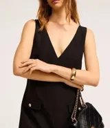 Vestido corto negro de crepé con escote en V tanto en la parte delantera como en la trasera. Tiene bolsillos delanteros con botones dorados.