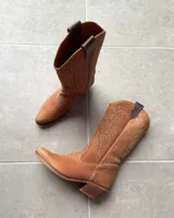 Bota estilo tejana de cuero vacuno color tostado, con costuras decorativas en contraste en la caña y taco bajo.
