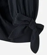 Blusa negra de viscosa con escote off-shoulder, mangas 3/4 con elásticos y lazos en los puños.