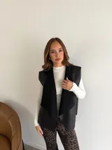 Chaleco de eco cuero marrón con interior y solapas de corderito sintético en color beige. Presenta un diseño sin mangas con corte recto y estructura abierta.