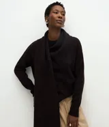 Suéter de punto color negro con fit holgado, mangas largas, cuello alto y bufanda integrada con caída frontal. Presenta puños y ruedo acanalados.