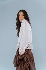 Camisa de lino blanca con detalles de encaje crochet en los puños y en el ruedo. Presenta un diseño romántico con cierre frontal de botones.