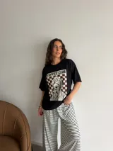 Remera oversize de algodón negro, con diseño gráfico frontal que incluye la leyenda "COFFEE CLUB" y una ilustración estilo retro de una mujer bebiendo café.