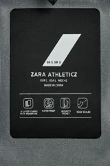 Cazadora deportiva de esquí con diseño bicolor en tonos negro y verde oliva. Presenta capucha amplia con visera, cierre frontal con cremallera termosellada, bolsillos frontales y en manga con cierres impermeables, y aberturas de ventilación en las axilas. Incluye faldón interior antinieve, puños ajustables y tecnología de rescate RECCO.