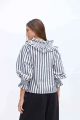 Blusa blanca de algodón con cuello alto fruncido con volados y mangas abullonadas con puños elásticos.