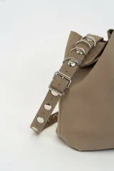 Bolso tipo shopper de gamuza marrón, con asa de hombro ajustable decorada con ojales metálicos plateados y hebilla lateral.