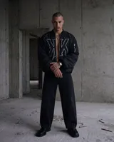 Campera bomber negra mate con diseño puffer, confeccionada en nylon impermeable. Presenta un gran logo bordado en color blanco en el frente, cierre frontal metálico, puños y bajo con elástico interno, y detalles de cierres en las mangas.