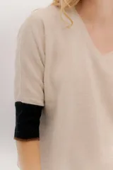 Buzo de punto en color negro con mangas tres cuartos y puños en contraste color marrón. Presenta un diseño holgado con tajos laterales y un aplique circular con logo en la parte inferior.