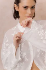 Camisa blanca de calce relajado con tejido semitransparente y bordados florales en relieve. Cuenta con cuello camisero, abotonadura frontal y mangas amplias.