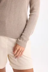 Sweater de punto color beige con hilos de lurex, escote en V y mangas largas con costuras en los hombros.