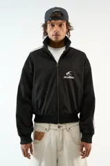 Campera de gamuza negra con cuello alto, cierre frontal completo con tirador personalizado y bolsillos laterales. Presenta bandas blancas laterales en las mangas y logo de la marca bordado en el pecho.