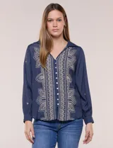 Camisa de estilo boho, color verde, con cuello camisero, escote en V y botonadura frontal con botones perlados. Cuenta con una pechera con bordados geométricos y florales a contraste, mangas largas abullonadas con puños abotonados y delicados bordados dispersos.