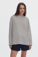 Remera manga larga de corte holgado, con diseño a rayas horizontales en tono blanco y negro, escote bote, pequeño bordado celeste en el pecho y estampa en la manga.