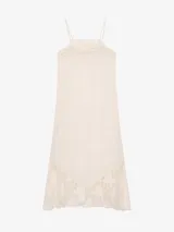 Vestido largo de lino color blanco, con finos breteles regulables, detalles de encaje en el escote y en el ruedo asimétrico, y silueta recta.