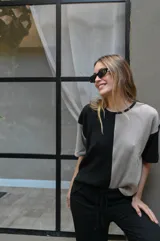 Remera de tejido de punto, manga corta, con diseño bicolor en negro y beige. La prenda es de corte holgado y presenta un ligero acanalado vertical.