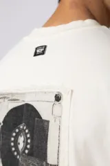 Remera negra de corte oversize confeccionada en tela pesada. Presenta un bordado frontal con la palabra 'REWIND' y un diseño de parche en la espalda con estética de papel roto.
