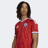 Camiseta de fútbol Adidas de la Selección Chilena, modelo local 26, color rojo con patrón de chevrons en relieve. Presenta cuello en V con ribete blanco y azul, y ribetes blancos en las mangas. Incluye el escudo de la federación chilena y el logo de Adidas en blanco.