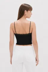 Musculosa de punto blanco, corte crop, con tirantes finos, escote en V adornado con detalles de encaje y un pequeño lazo en el centro.