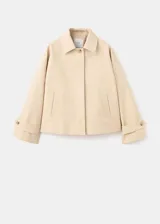 Chaqueta de corte recto y holgado color beige, con cuello clásico, cierre frontal de botones marrones, bolsillos de ojal laterales y puños ajustables con presillas.