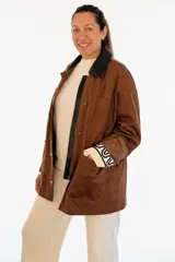 Campera de ecocuero color chocolate, con diseño amplio y relajado. Presenta cuello camisero, cierre frontal con cremallera y botones a presión, además de bolsillos delanteros amplios.