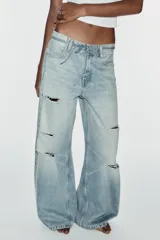 Jeans de tiro medio y corte baggy con cinco bolsillos, trabillas y rotos decorativos. Cuenta con detalle de cinturón confeccionado en el mismo tejido y cierre frontal con cremallera y botón metálico.
