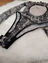 Body de manga larga y cuello alto, confeccionado en microtul estampado con diseño animal print abstracto. Presenta una espalda descubierta y cierre con broches en la entrepierna.