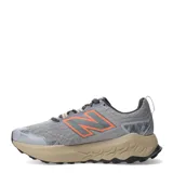 Championes de trail running New Balance modelo Garoe, color gris con detalles en naranja y suela en tono arena. Presentan tecnología Fresh Foam en la entresuela para mayor amortiguación y refuerzos en la puntera para mayor protección.
