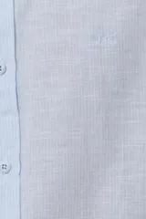 Camisa de manga larga confeccionada en mezcla de lino y algodón, con sutiles rayas celestes, cuello camisero clásico y cierre frontal de botones.